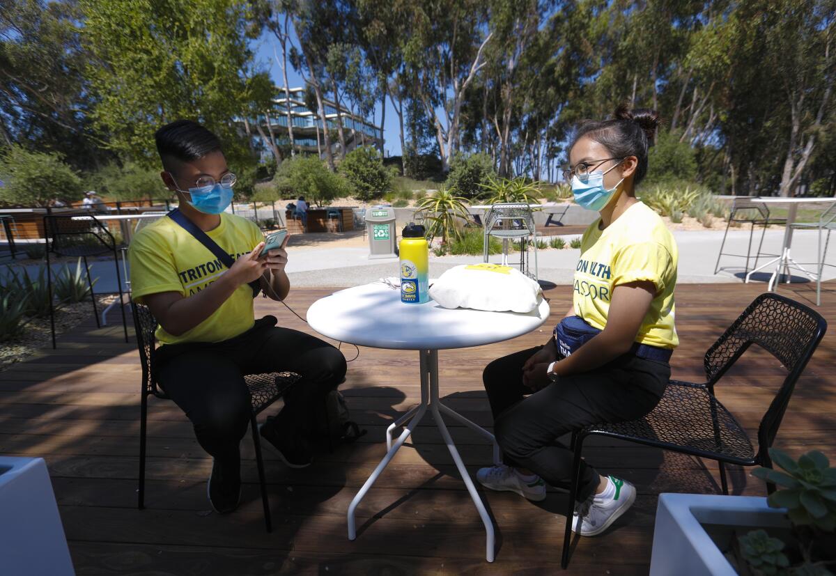UCSD student Luan Nguyen, left, and his sister, Diep Nguyen, try out the  COVID-19 exposure app sitting at an outdoor table