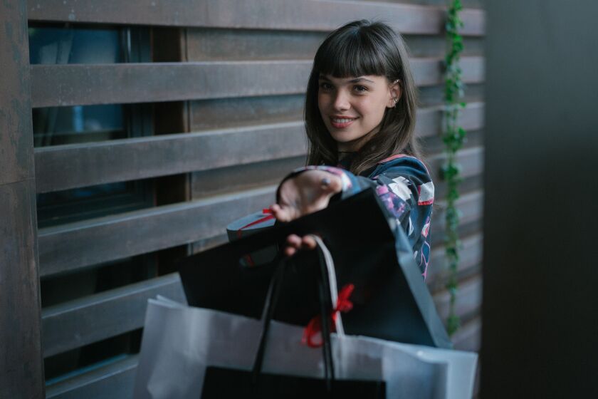 A teenage girl holds out gift bags, smiling