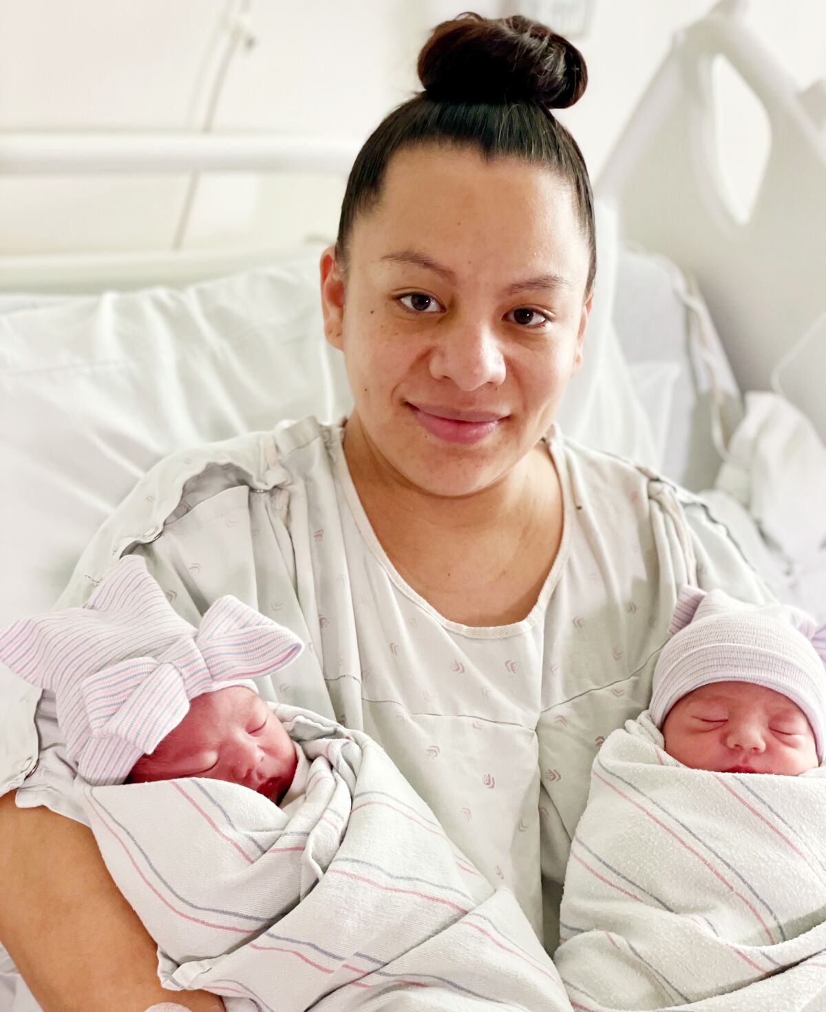 A woman smiles in a hospital bed with twins in each arm
