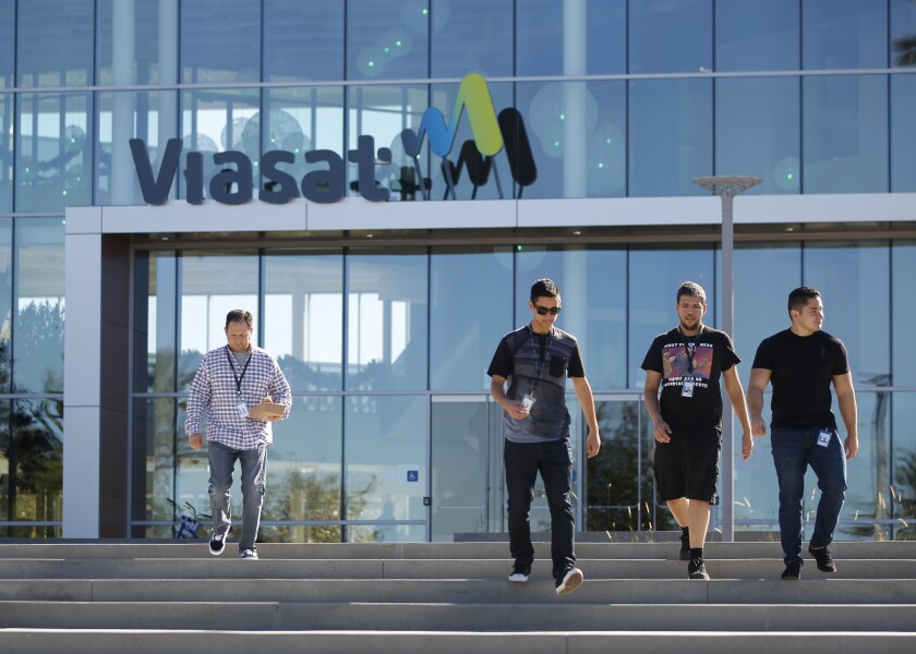 Employees walk in front of Viasat's campus in Carlsbad .  