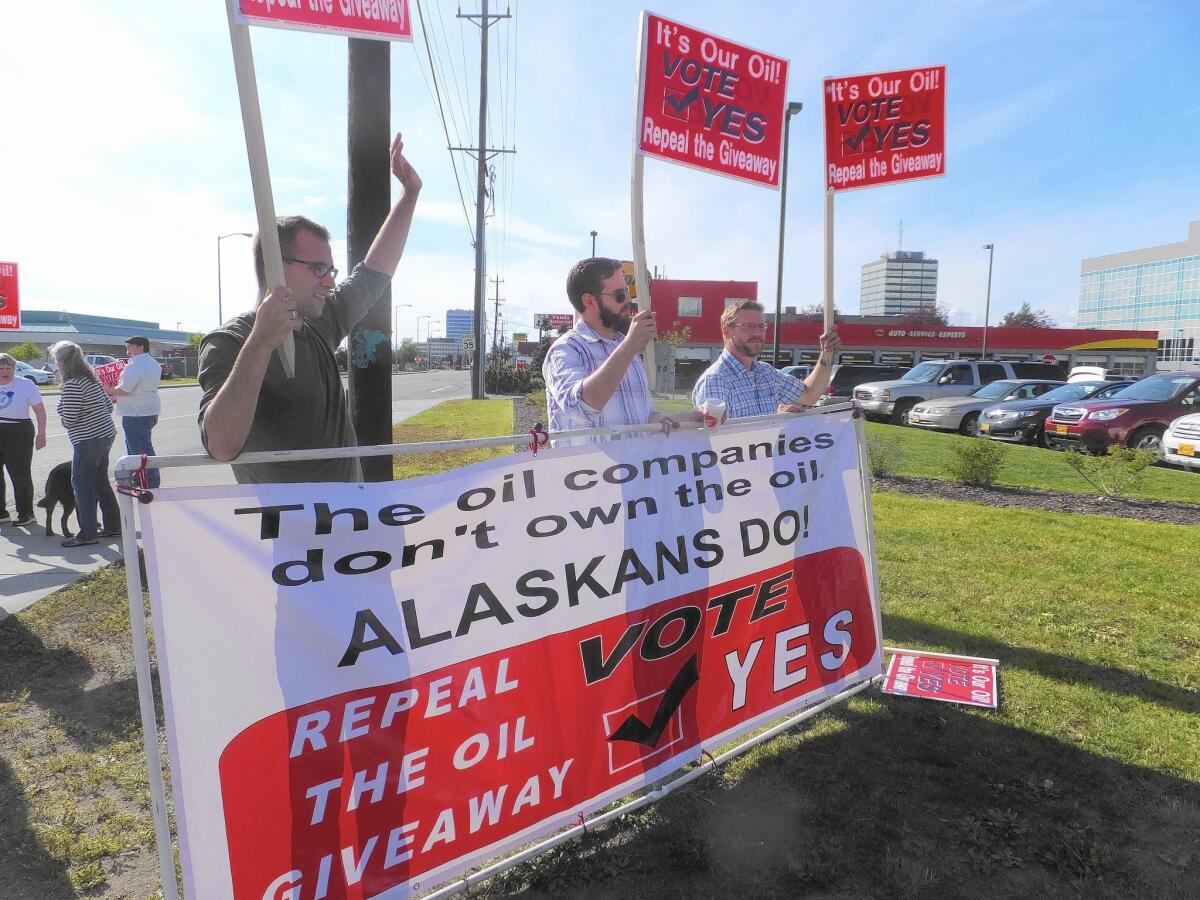 Supporters of an effort to repeal oil tax cuts approved by the Alaska Legislature in 2013 wave signs along an Anchorage street in August.