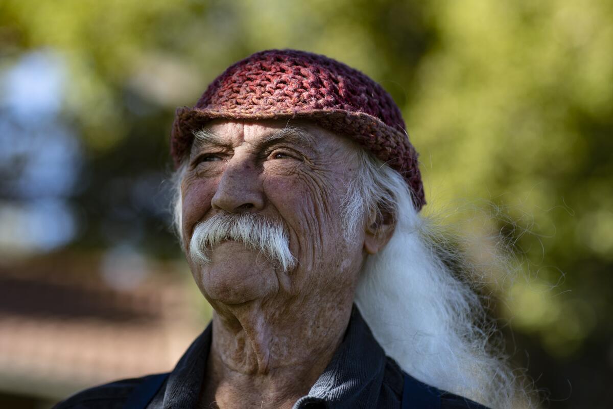 A man with long white hair and a bushy white mustache looks off into the distance.