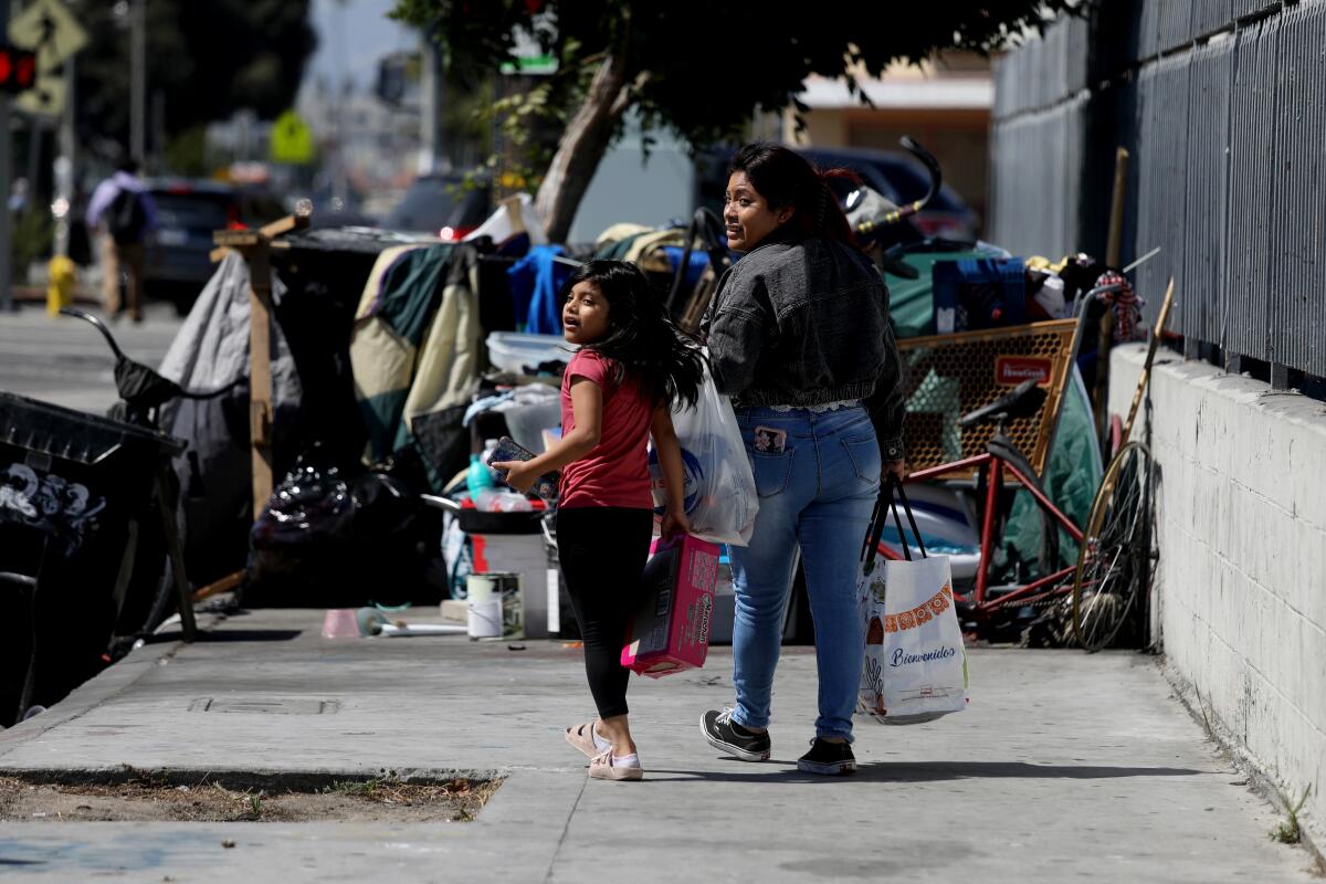 A young girl and a woman look before walking into the street to get around a homeless encampment 