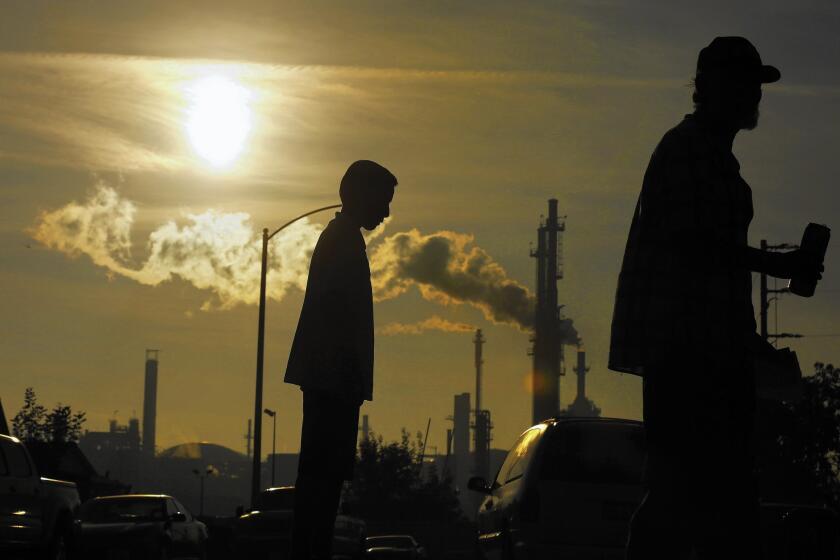 Jesse Ceja and his grandfather, Paulo Torres, 69, stand on Emden Street in Wilmington, where they live next to the Phillips 66 refinery seen in the background.