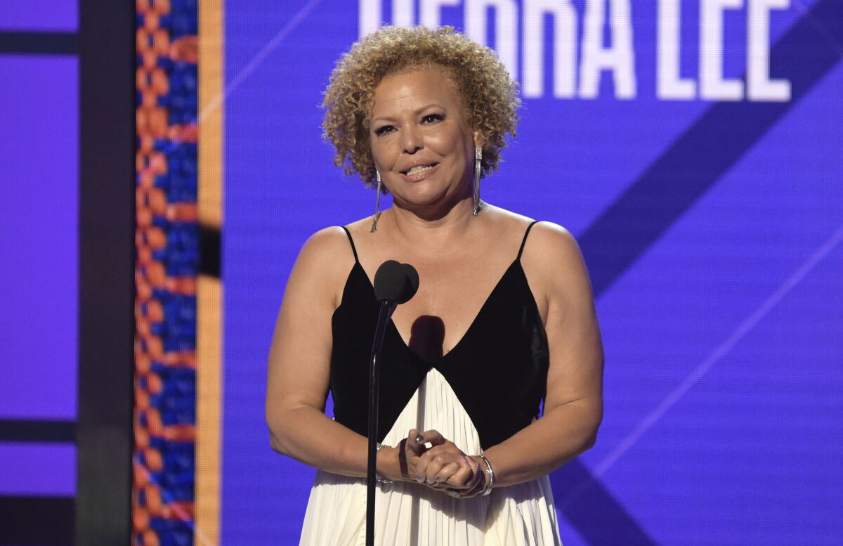 A woman with short curly hair with her hands clasped stands onstage