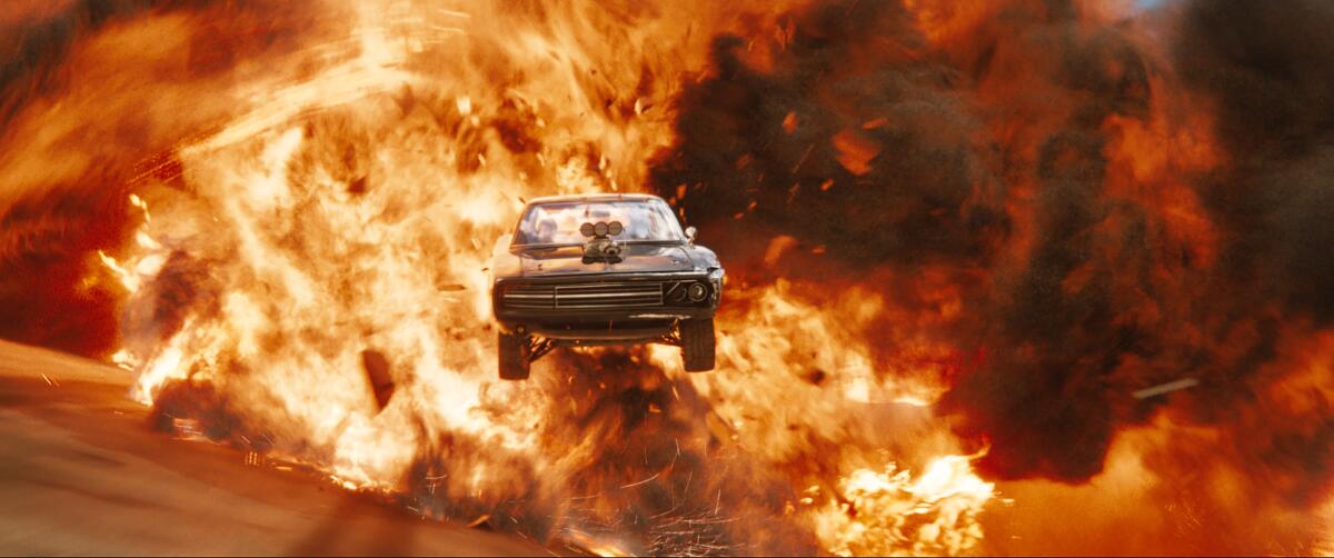 An airborne muscle car emerges from a wall of flames