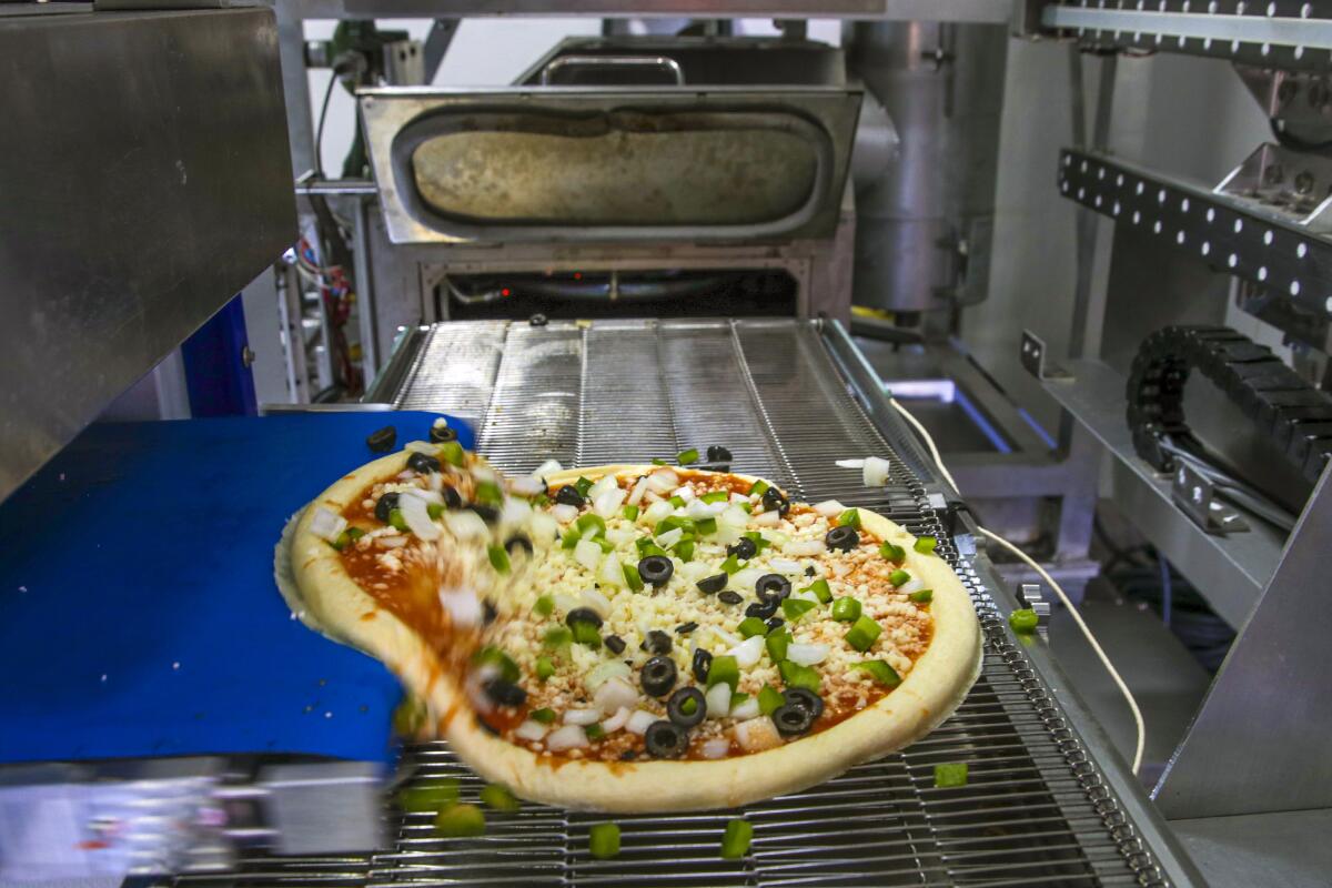 A pizza with toppings comes off the conveyor belt inside the pizza robot.
