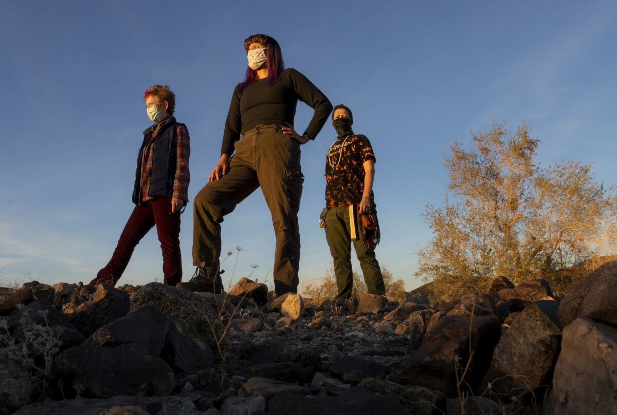 Ellen Mackey, Gina Chavez and Lee King pose for a portrait standing on rocks in a desert landscape