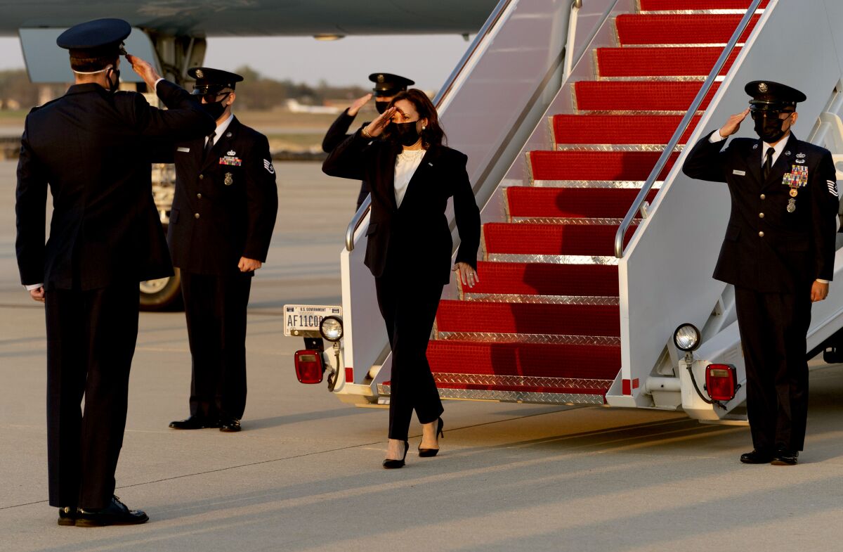 Kamala Harris salutes as she exits a plane with military members in uniform nearby