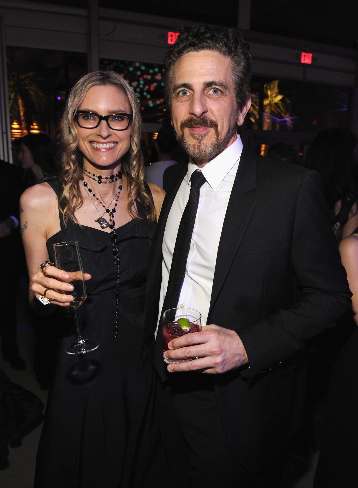 A woman in a dress, left, and a man in a suit, both holding glasses