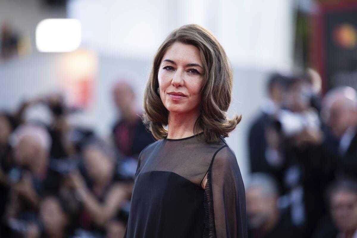 Sofia Coppola poses for photographers in a black gown with blurred figures in the background