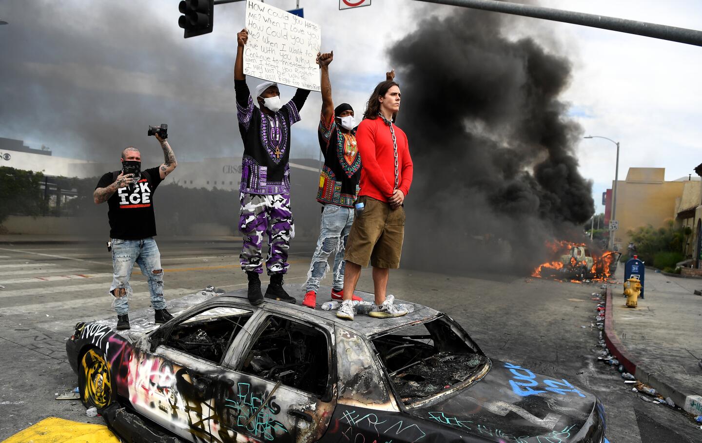 Protestors stand on top of a burned LAPD cruiser as another burns at 3rd Street and Fairfax Avenue in Los Angeles on Saturday.
