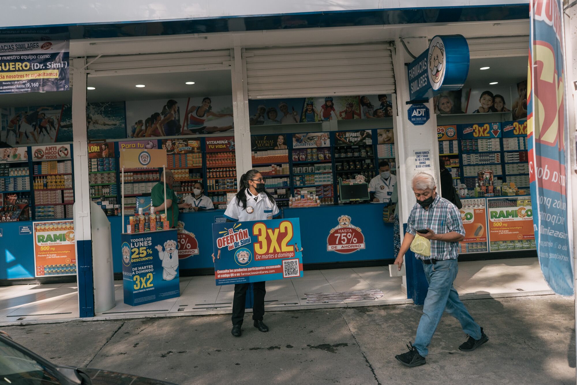 A woman holds a blue sign outside a storefront, near a passerby