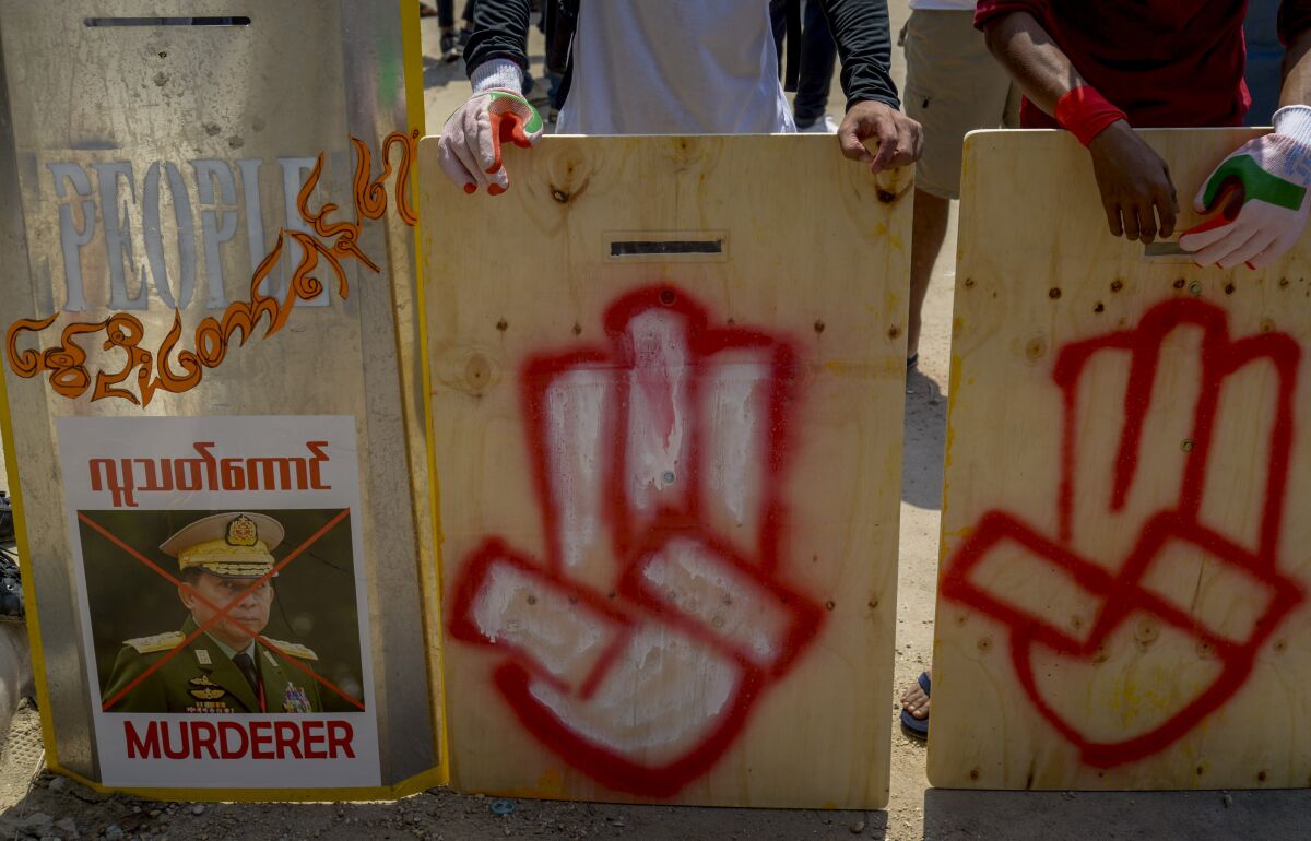 Anti-coup protesters stand behind a line of makeshift shields marked with three-fingered salute