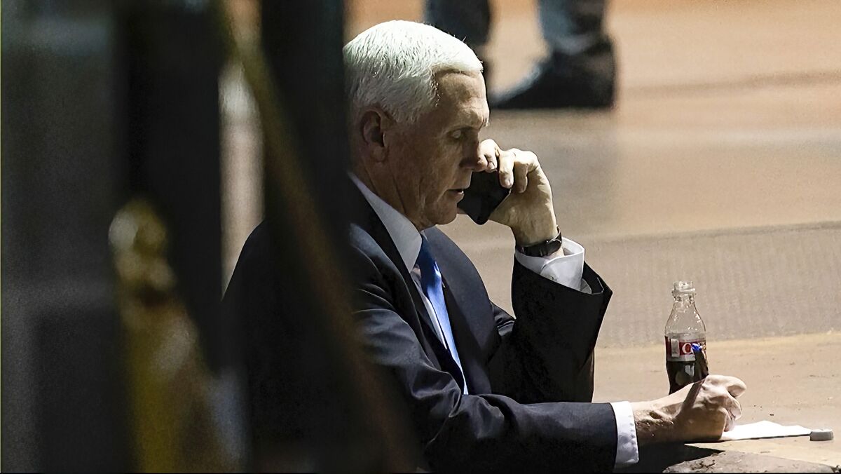 Vice President Mike Pence writes on a piece of paper while on his cellphone.