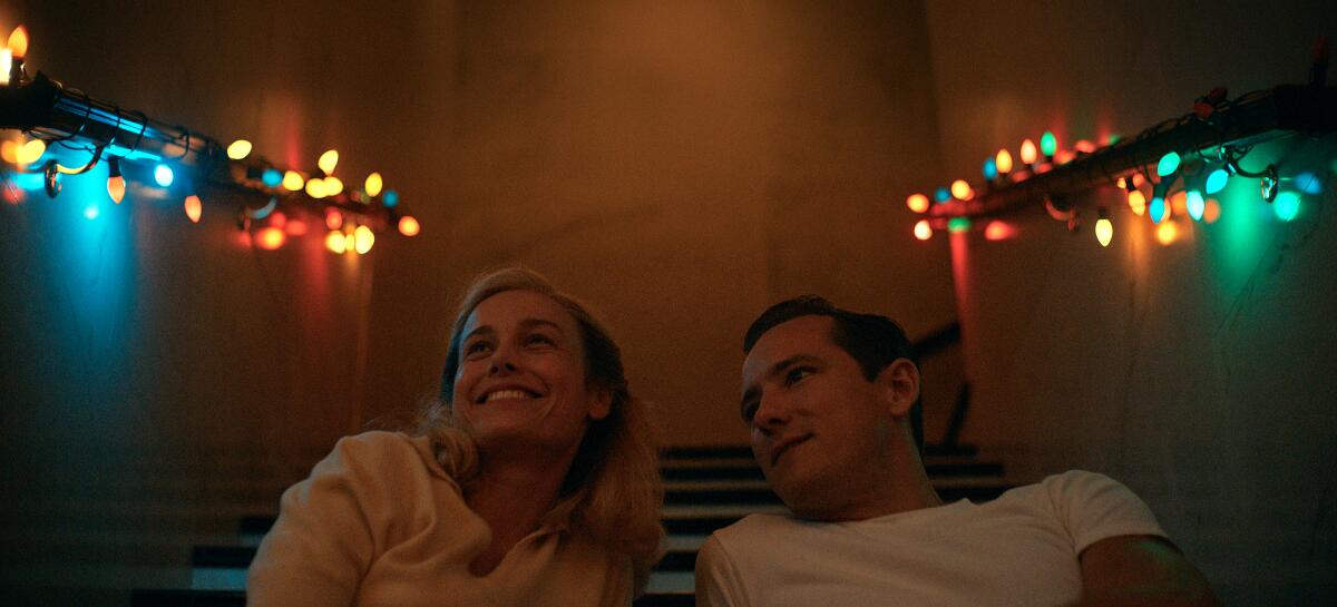 Actors Brie Larson and Lewis Pullman sit closely in a scene from "Lessons in Chemistry."