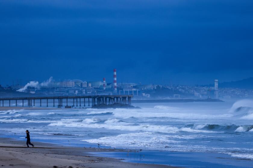 Santa Monica, CA - March 31: A runner jogs along the sand as waves roil the ocean along empty beach where a late season storm begins to move out of Southern California on Sunday, March 31, 2024 in Santa Monica, CA. (Brian van der Brug / Los Angeles Times)