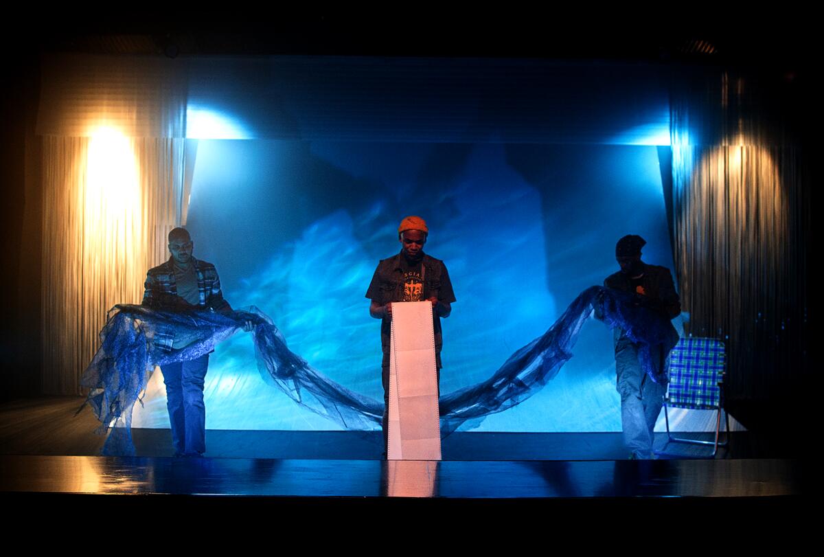 A man speaks from a lectern between two other men holding a shroud 