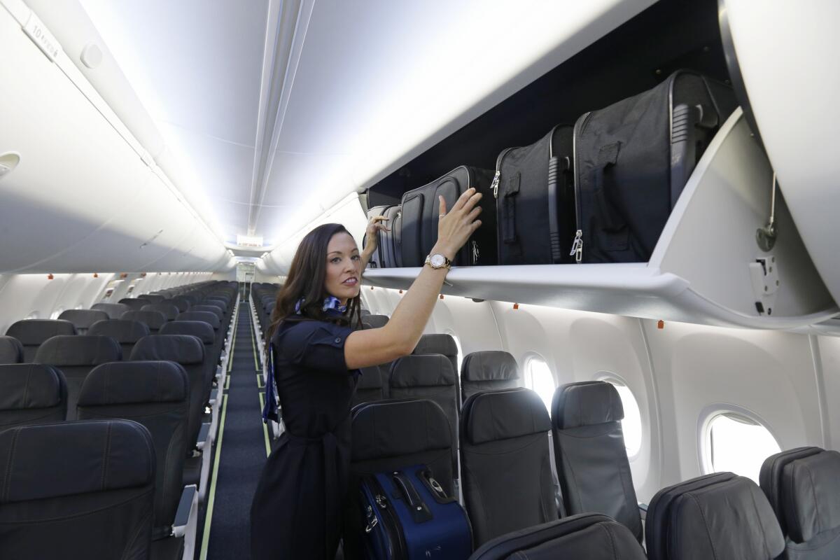 Flight attendant Jenn-Marie Mann shows how carry-on roller bags fit up on their sides in new larger luggage bins installed on an Alaska Airlines 737-900ER airplane.
