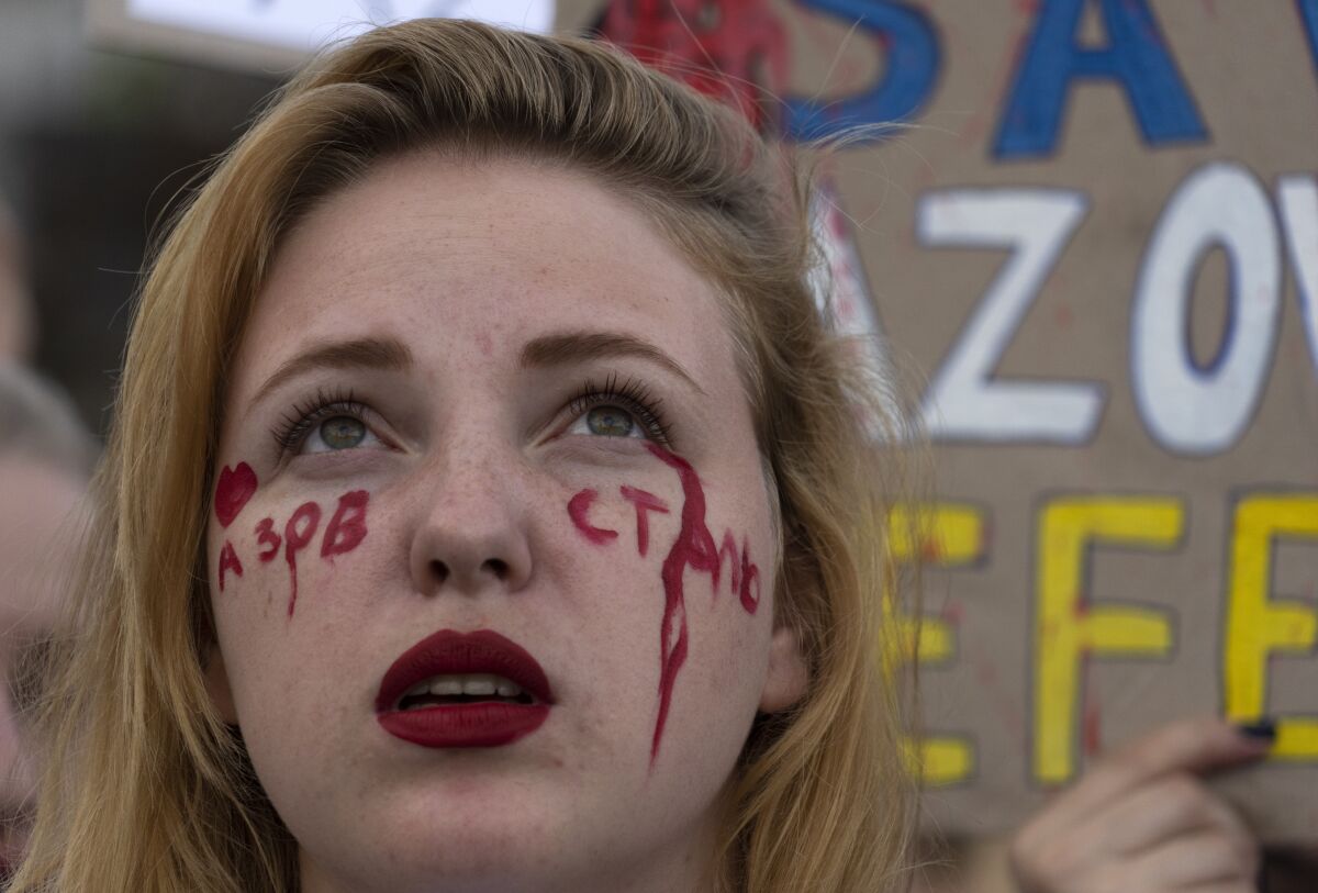 A relative with the writing 'Above Steel' on her face attends a rally in support of Ukrainian soldiers from the Azov Regiment who were captured by Russia in May after the fall of Mariupol, in Kyiv, Ukraine, Thursday, Aug. 4, 2022. The rally comes as U.S. officials believe Russia is working to fabricate evidence concerning last week's deadly strike on a prison housing prisoners of war in a separatist region of eastern Ukraine. (AP Photo/Efrem Lukatsky)