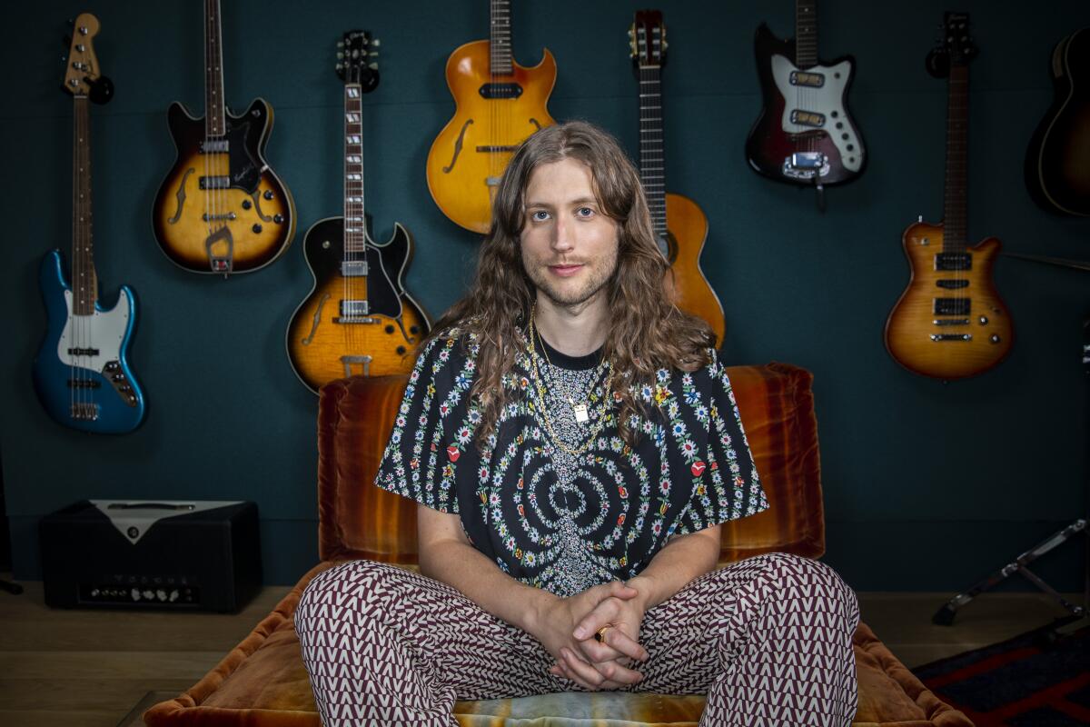 Portrait of Ludwig Göransson backed by a wall mounted with guitars  