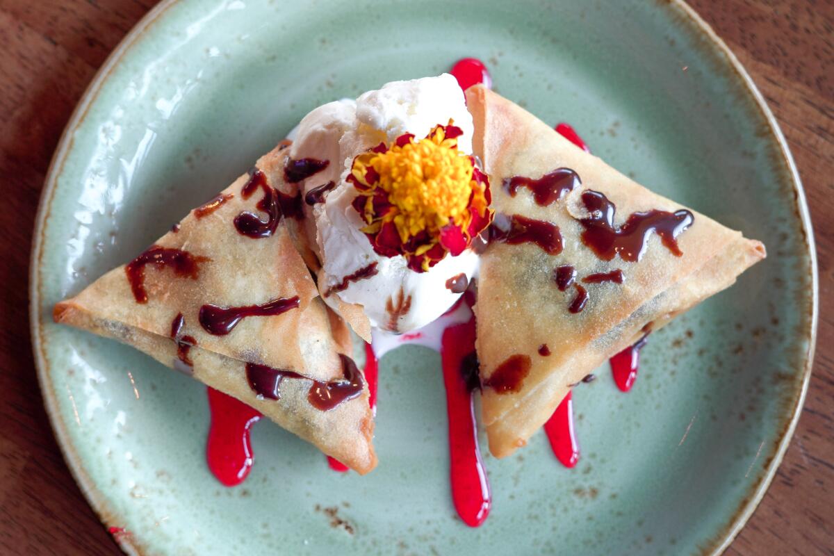 Two triangular samosas, drizzled with colorful sauces, on a turquoise ceramic plate.