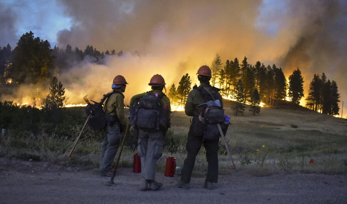 Firefighters watch a hillside burn on the Northern Cheyenne Indian Reservation, Wednesday, Aug 11, 2021, near Lame Deer, Mont. The Richard Spring fire was threatening hundreds of homes as it burned across the reservation. (AP Photo/Matthew Brown)