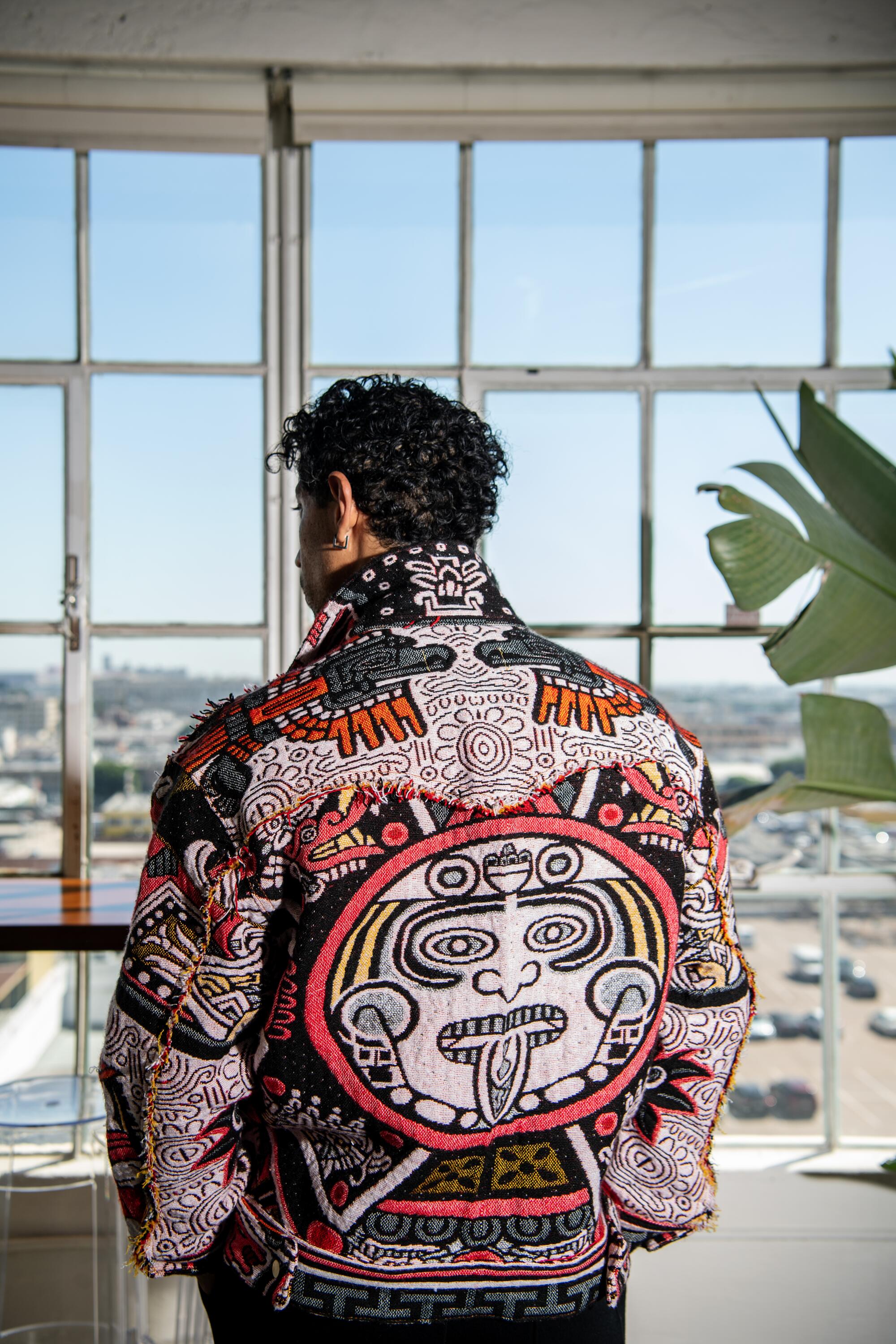 A man faces his back away from us so we can see the colorful geometric prints of his jacket.