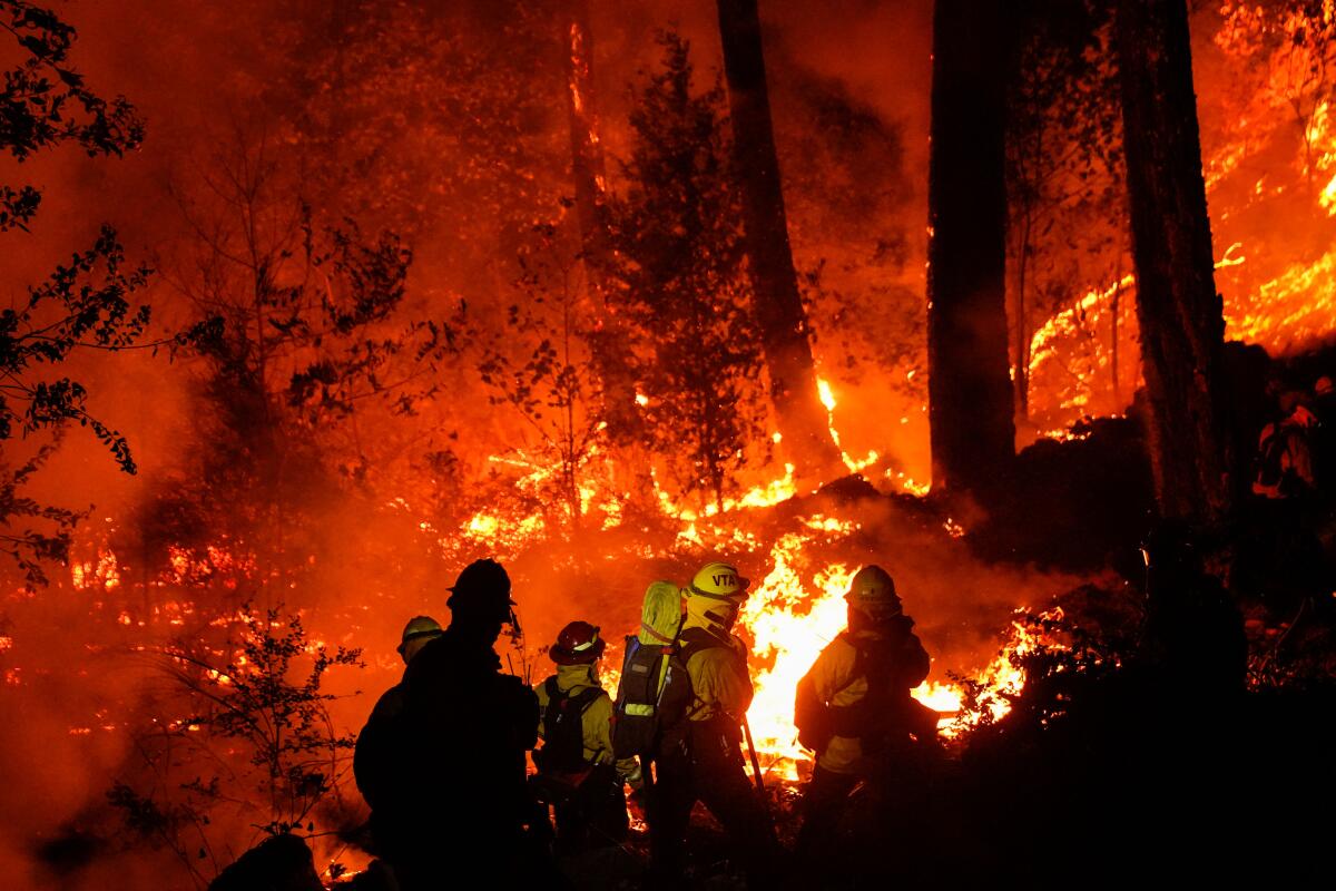 A crew fights a wildfire on a hill at night.