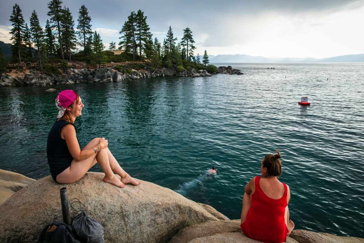 Two people sit on rocks on the shore of Lake Tahoe
