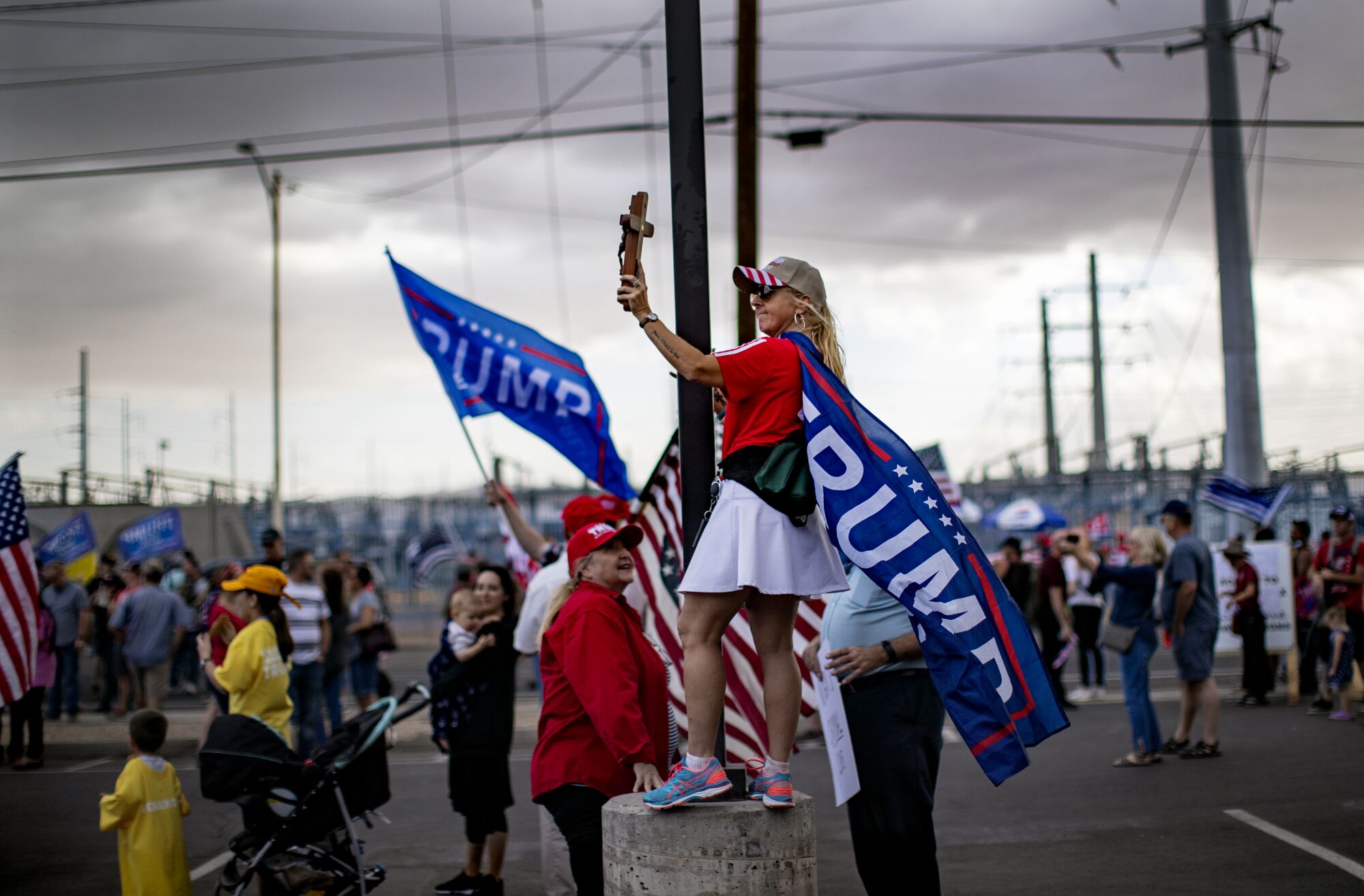 As storm clouds move in, a woman covered in Trump flags holds up a cross at a rally in Phoenix.