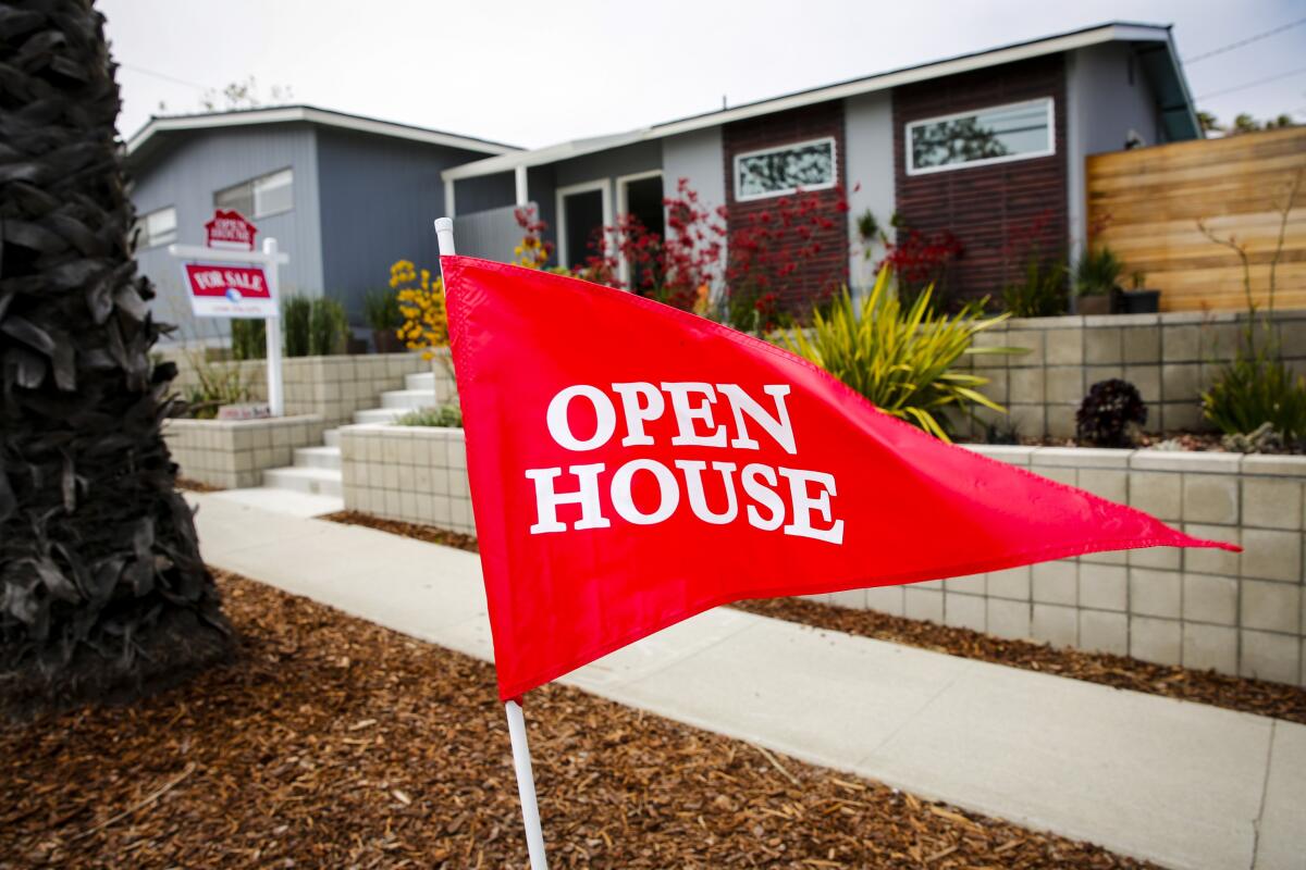 Closeup of a flag with the words "Open House" in front of a home with a For Sale sign.