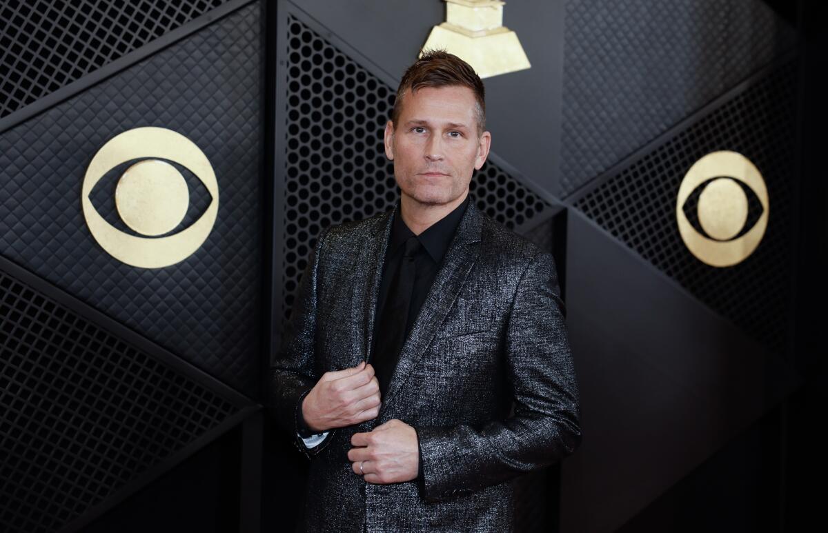 Kaskade wears a black shirt and holds the lapel of his metallic blazer while arriving at the Grammy Awards