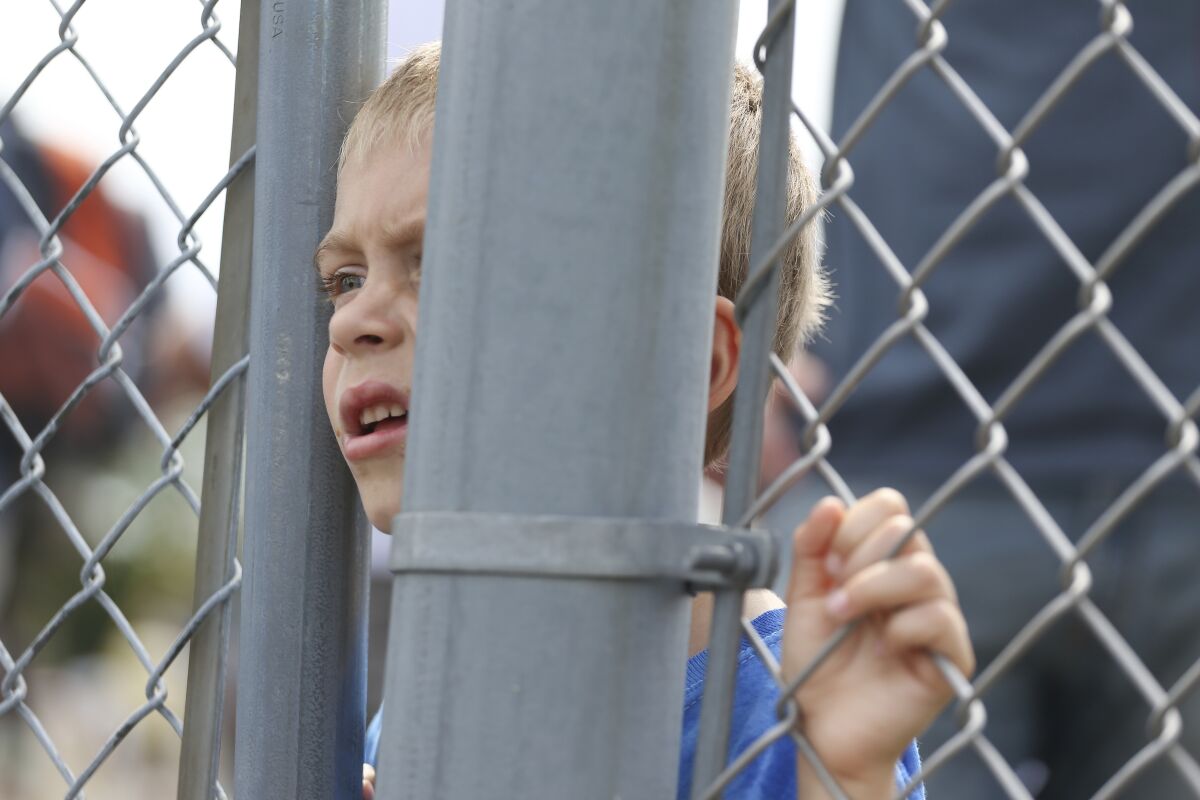 A young fan watches through the fence as pit crews move cars in the garage area before the NASCAR Xfinity Series auto race at Watkins Glen International in Watkins Glen, N.Y., on Saturday, Aug. 7, 2021. (AP Photo/Joshua Bessex)