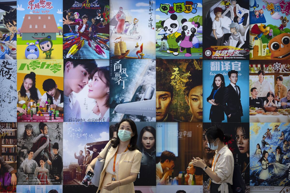 Visitors walk past a display of posters for Chinese movie and television productions at the China International Fair for Trade in Services (CIFTIS) in Beijing, Friday, Sept. 3, 2021. China's government banned effeminate men on TV and told broadcasters Thursday to promote "revolutionary culture," broadening a campaign to tighten control over business and society and enforce official morality. (AP Photo/Mark Schiefelbein)
