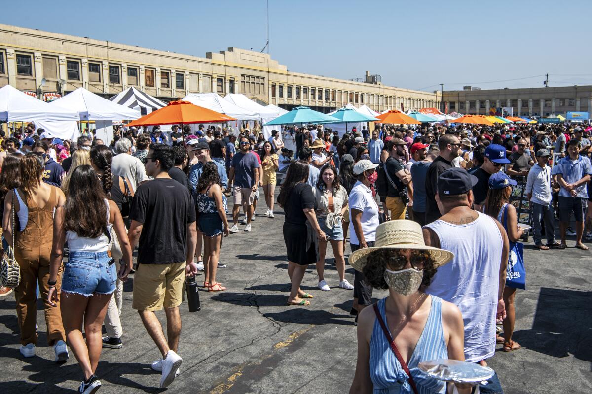 A crowd of guests on a sunny day at Smorgasburg; in the background, umbrellas and the tents of food stalls can be seen.