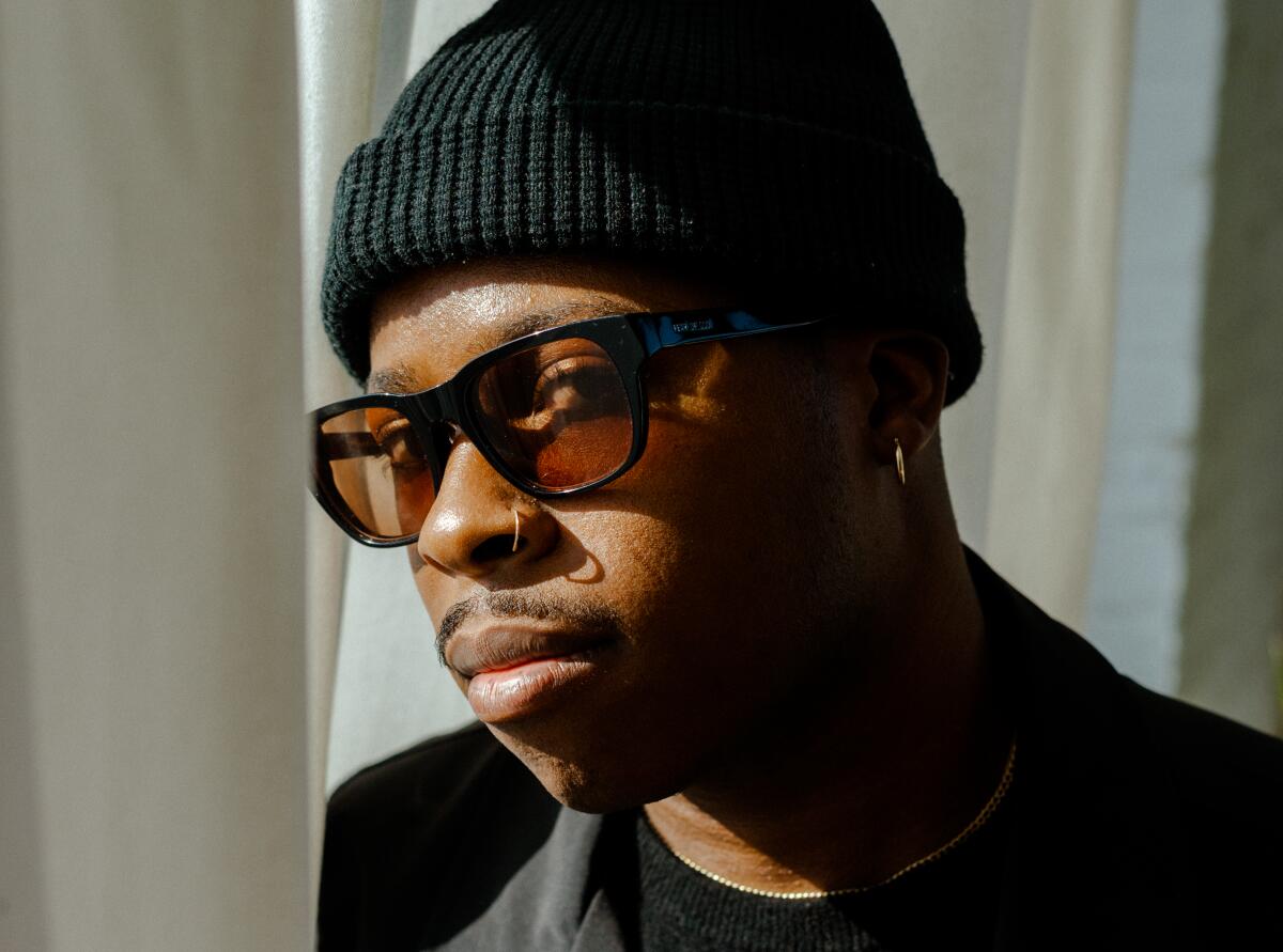 A profile view of a man in a black beanie and tinted glasses.