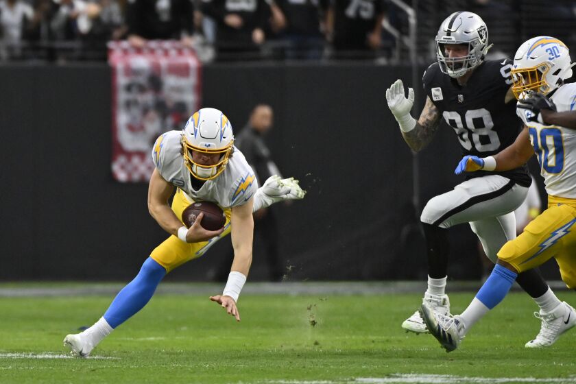 Los Angeles Chargers quarterback Justin Herbert (10) carries after picking up his fumble under pressure from Las Vegas Raiders defensive end Maxx Crosby (98) during the first half of an NFL football game, Sunday, Dec. 4, 2022, in Las Vegas. (AP Photo/David Becker)