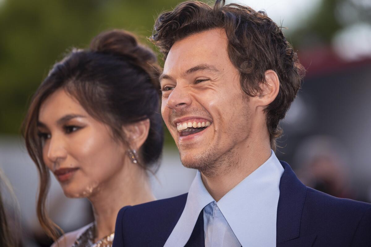 A young man in a suit laughs and a woman stands next to him