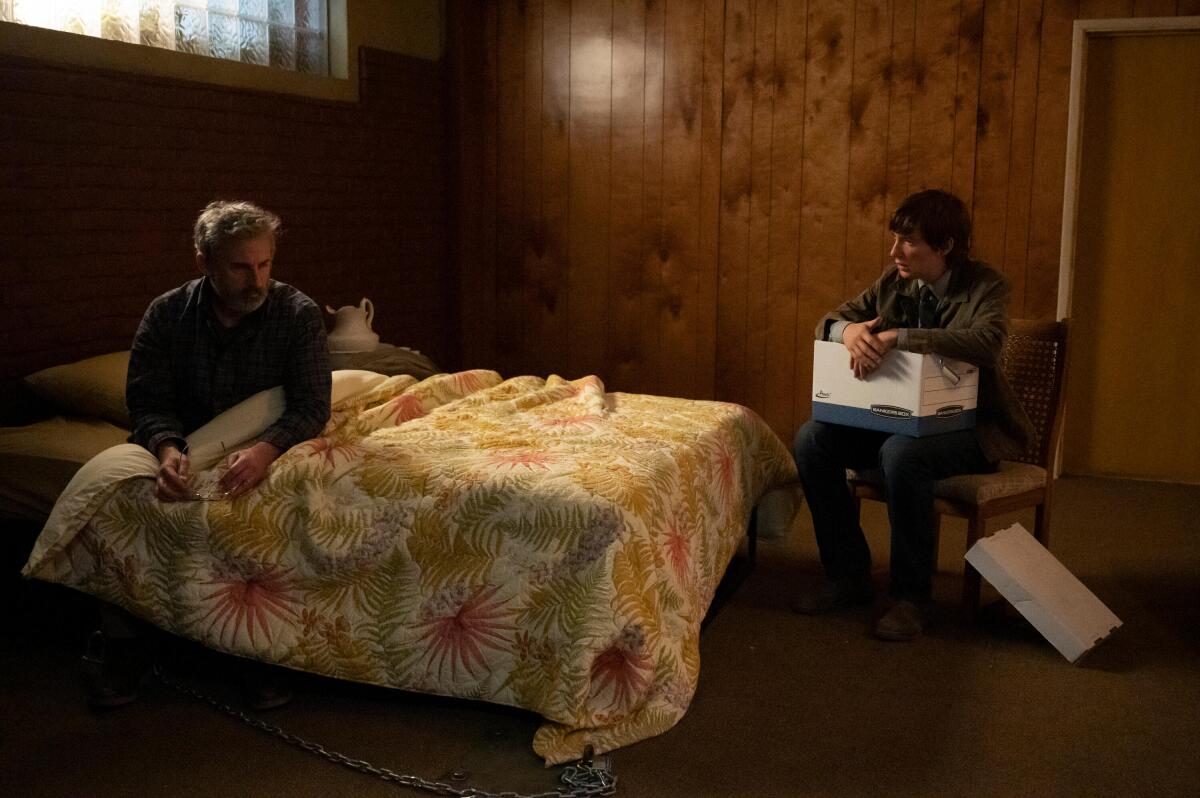 Steve Carell sits chained to a bed and Domhnall Gleeson sits out of reach on a chair in a scene from "The Patient."