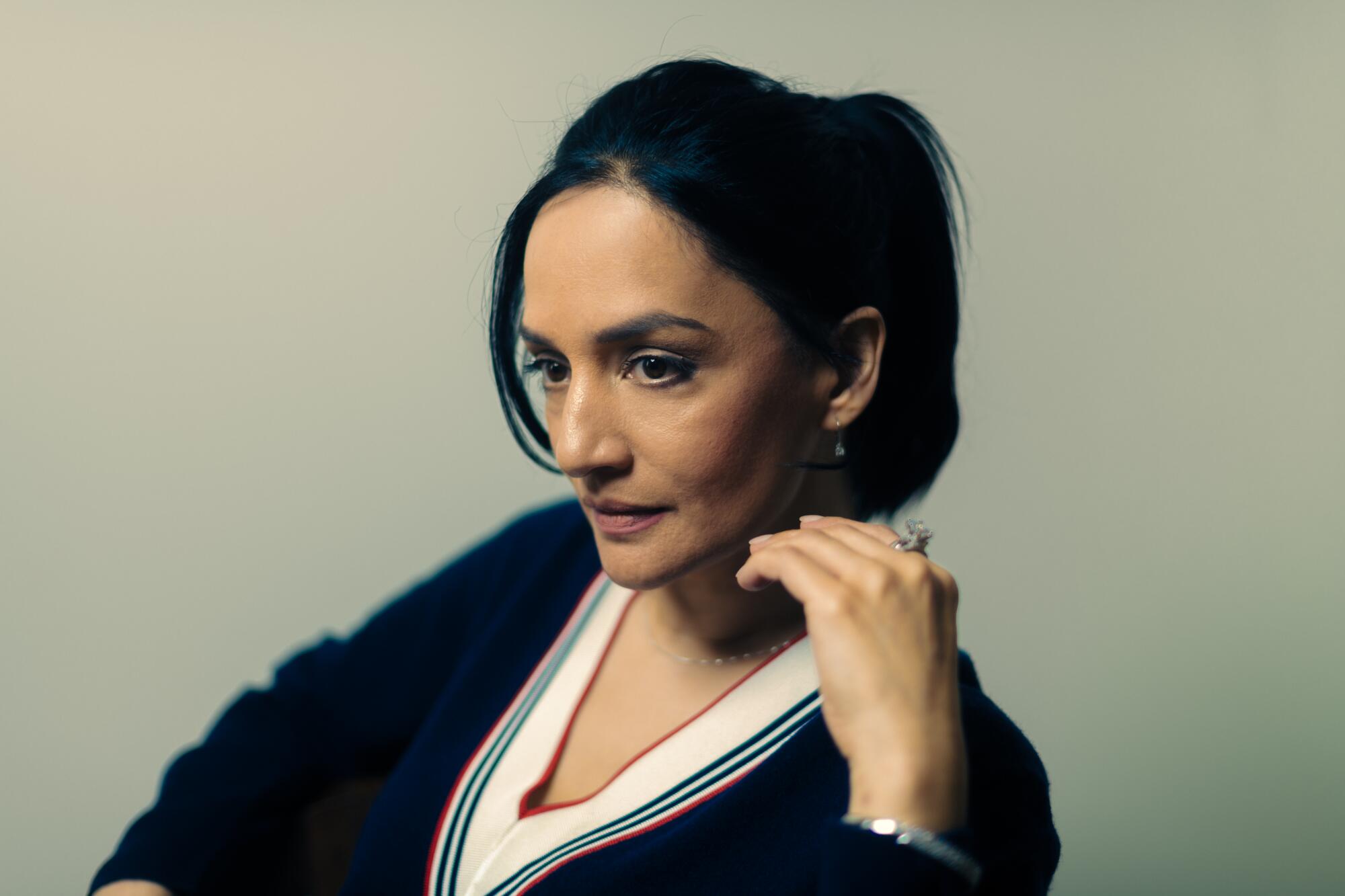 Archie Panjabi, from the shoulders up, in a dark dress with her hand near her face.
