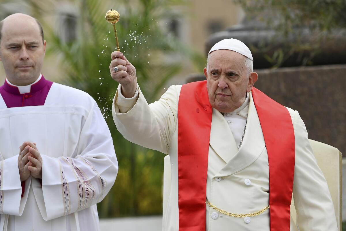 Pope Francis sprinkles holy water while wearing a white coat with a red stole.