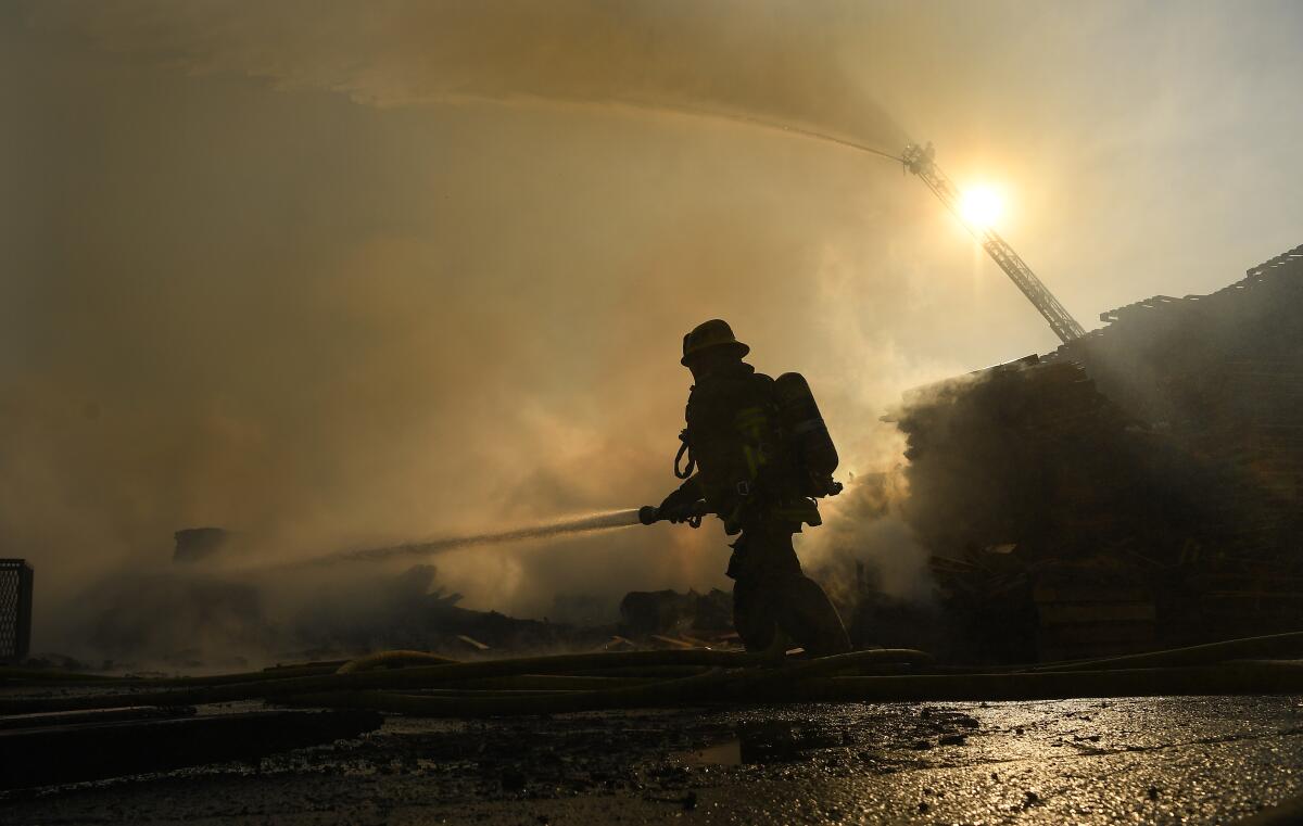 A firefighter sprays water as a fire engine in the background does the same