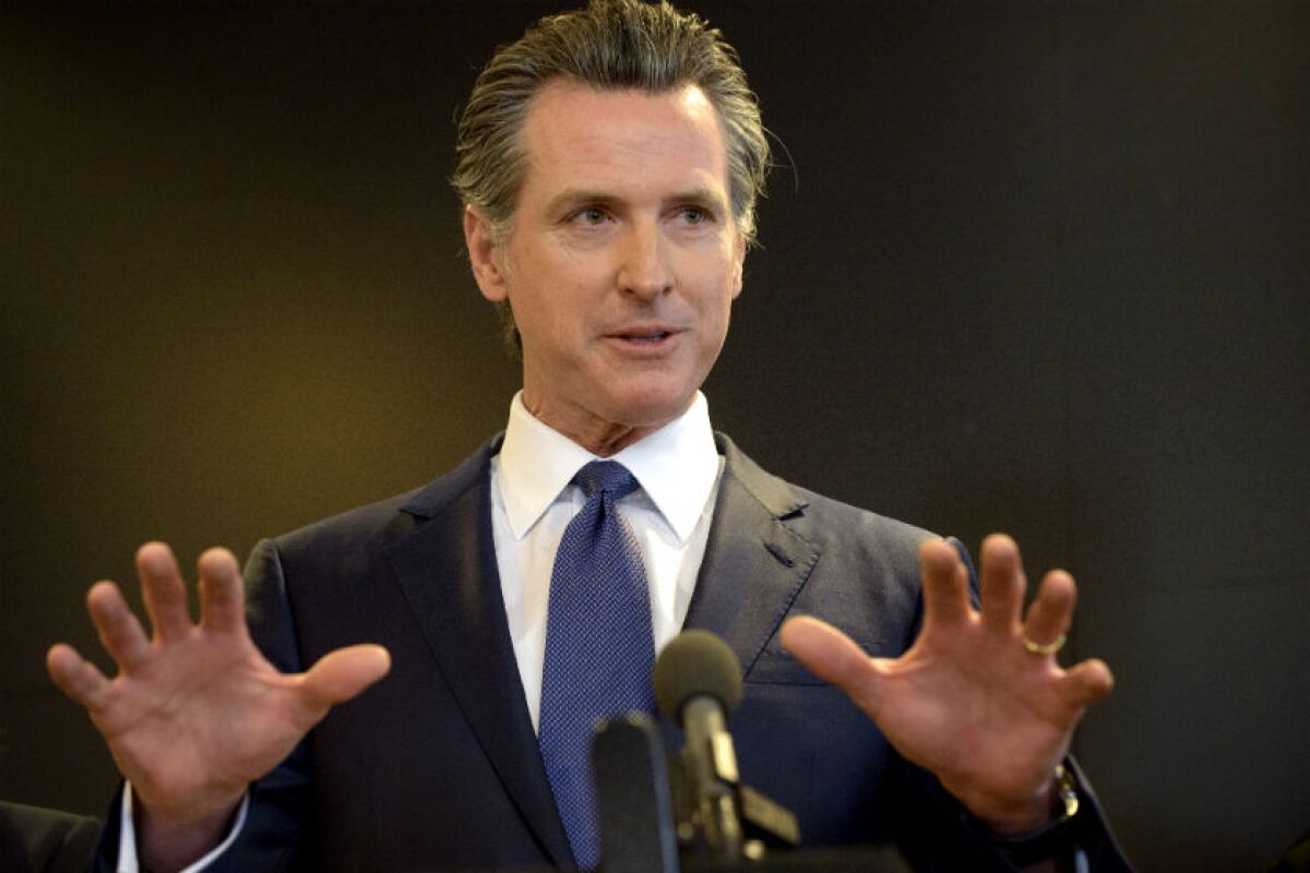 Gavin Newsom holds up his hands while speaking at a microphone.