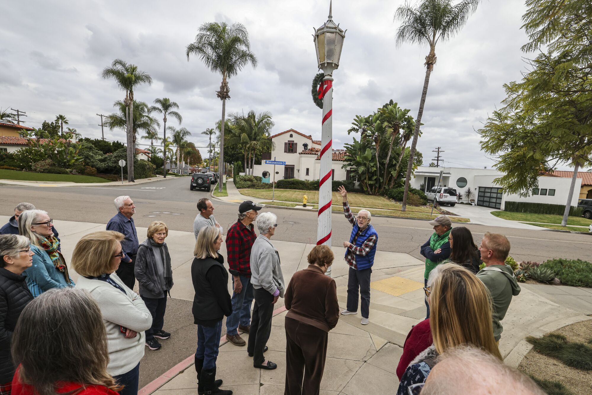 A group of people gathers around a historic streetlamp wrapped in ribbon and bearing a Christmas wreath.