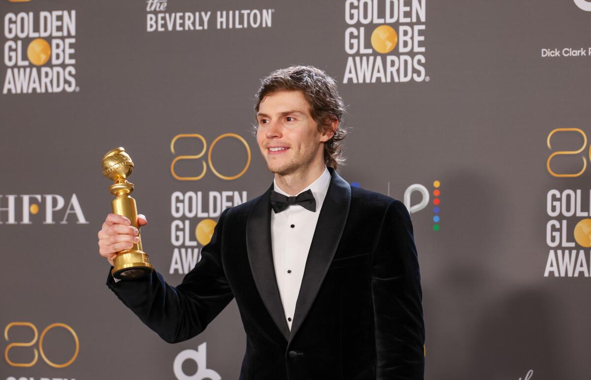 A smiling guy holds out his Golden Globe Awards.