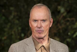 Michael Keaton poses for photographers in a tan polo and brown houndstooth blazer