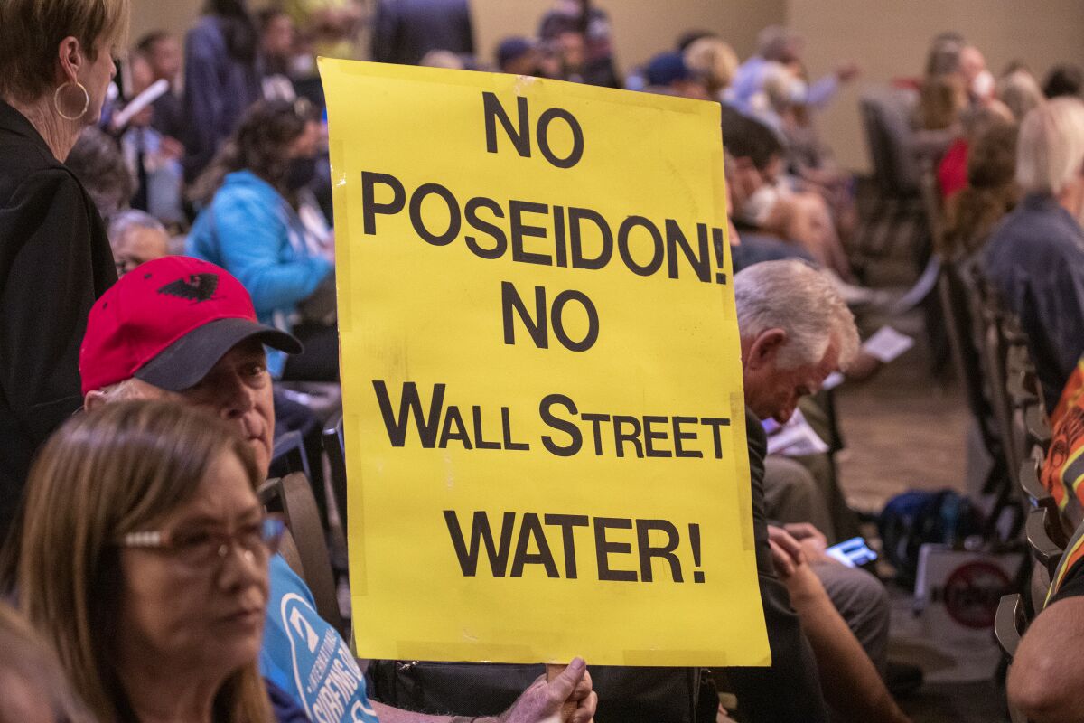 Opponents of a proposed desalination plant attend a meeting, with one carrying a yellow sign. 