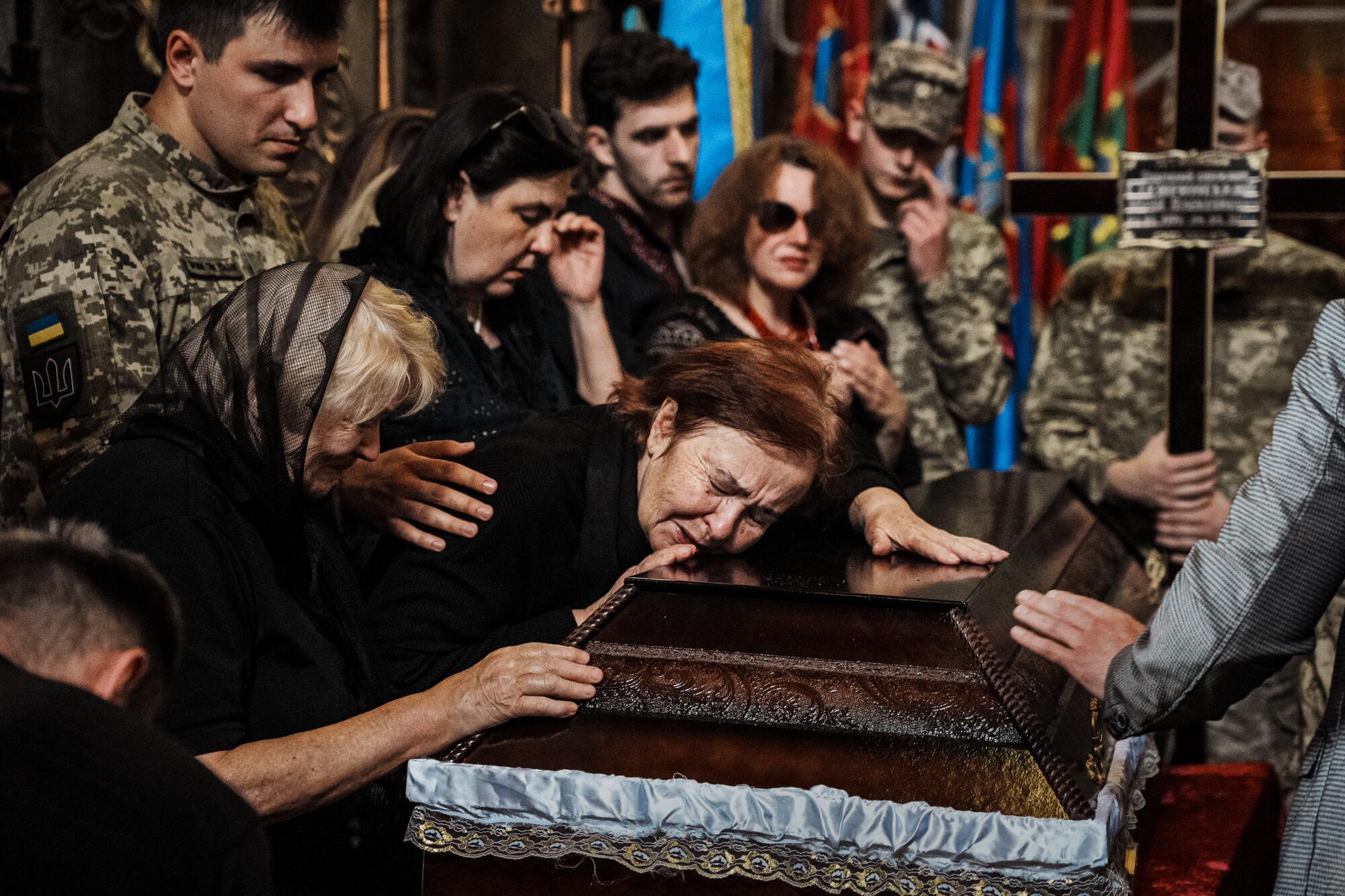 A woman rests her head on a casket. She is surrounded by other mourners. 