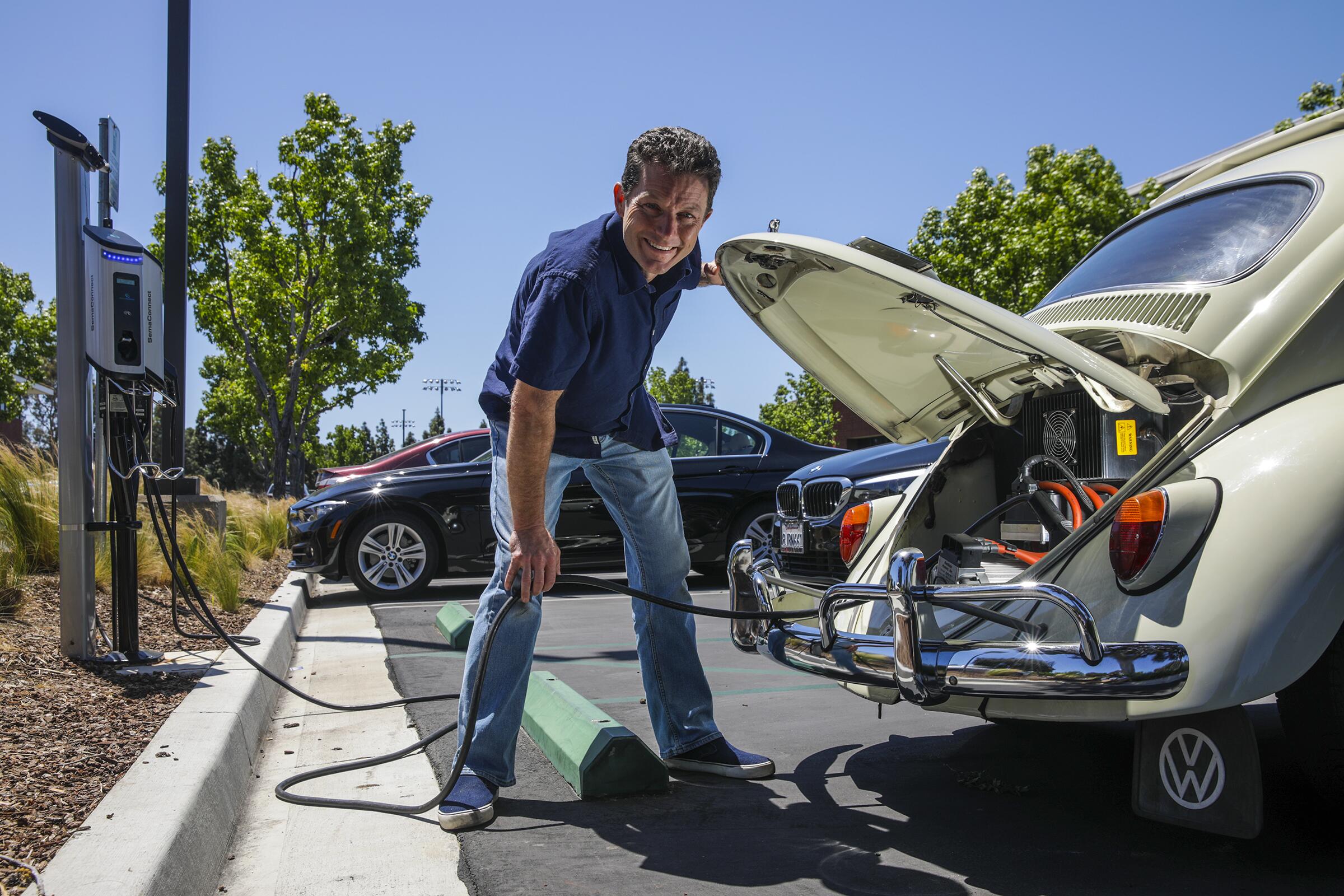 A man charges a Volkswagen Beetle that has been converted into an electric vehicle.